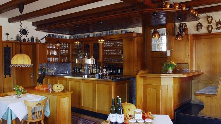 Een gezellige, rustieke bar met houten meubels en een toonbank. Op de tafels staan flessen wijn en glazen, terwijl de muren versierd zijn met oude decoraties.