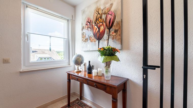 Een uitnodigende gang met een houten tafel, waarop een vaas met bloemen staat. Aan de muur hangt een decoratief schilderij met bloemmotieven.