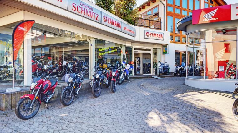Ein Motorradgeschäft mit verschiedenen Motorrädern vor einem hellen Gebäude. Die Marken Honda und Yamaha sind deutlich sichtbar.
