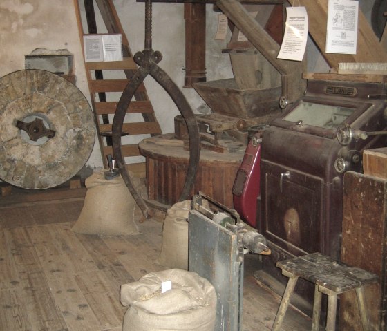 Innenansicht einer alten Mühle mit Mühlsteinen, Getreidesäcken und Holzkonstruktionen. Ein traditionelles Mühlenambiente mit rustikalen Elementen., © Peter Gillig