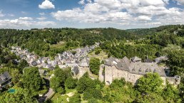 Panoramablick auf Monschau mit der Burg im Vordergrund, umgeben von gr&uuml;ner Landschaft und bewaldeten H&uuml;geln unter blauem Himmel mit Wolken., &copy; Eifel Tourismus GmbH, Dominik Ketz