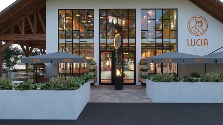 A modern building with large windows and an inviting entrance. Outside, there are tables with umbrellas, and flower beds are decoratively arranged.