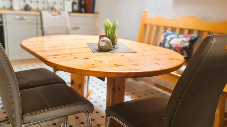 A round wooden table stands in a cozy kitchen. Around it are black chairs and a wooden bench.