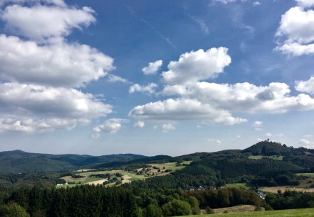 Wide landscape with green hills, forests and fields. The ruins of Nürburg Castle can be seen on a hill. The sky is blue with white clouds., © SebastianSchulte