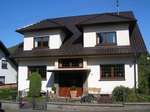 Een modern tweelaags huis met een wolfdak en bruine ramen. De entree is aantrekkelijk vormgegeven en er is een kleine tuin aan de voorkant.