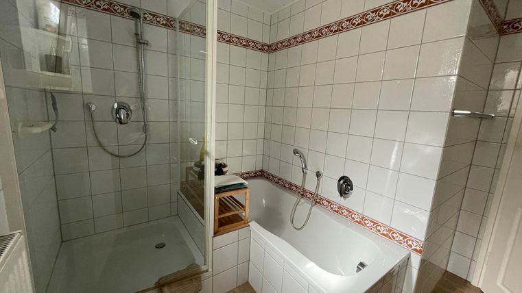 Een moderne badkamer met een douche en een bad. De wanden zijn betegeld en versierd met een decoratieve rand.
