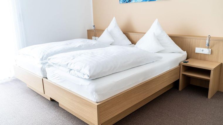 Een eenvoudige slaapkamer met een tweepersoonsbed en twee grote kussens. Naast het bed staat een nachtkastje.