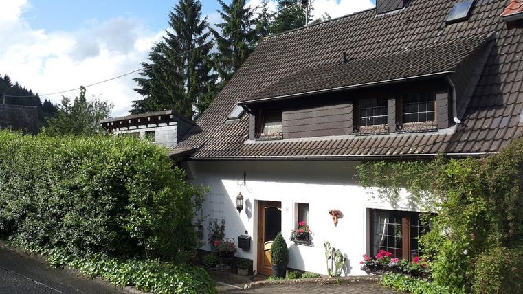 A charming house with a well-maintained garden. Surrounded by trees under a blue sky.