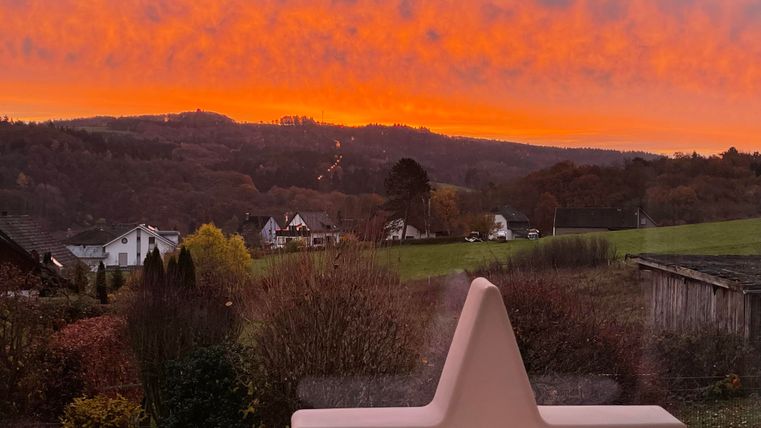 Un coucher de soleil à couper le souffle avec des nuages orange lumineux au-dessus de douces collines. Au premier plan, une étoile rose est visible en décoration.