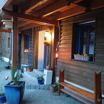 Een gezellige ingang van een houten gebouw met blauwe raamkozijnen. Planten en een houten bank verfraaien het gebied.