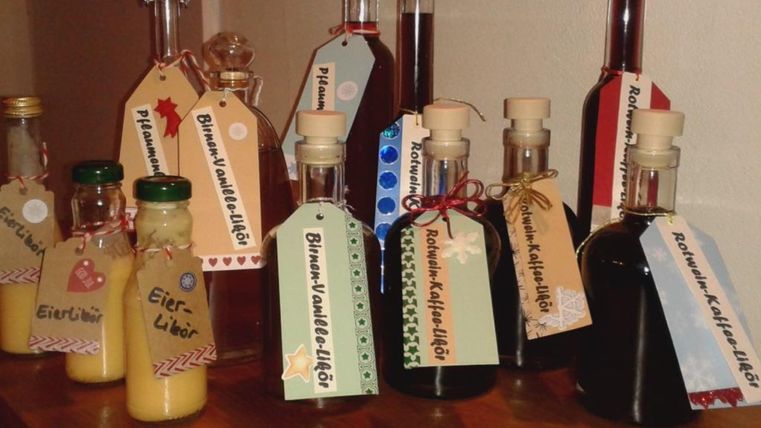 Eine Reihe von Flaschen mit verschiedenen Likören stehen auf einem Tisch. Jede Flasche hat ein Etikett mit einer Beschreibung des Inhalts.