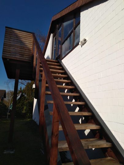 A wooden staircase leads to an upper entrance of a house. The sky is blue and beautiful.