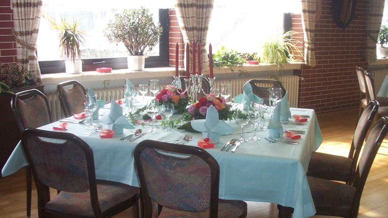 Een elegant gedekte tafel met een blauwe tafelkleed, glazen en bestek. Bloemenarrangement en kaarsen zorgen voor een feestelijke sfeer.