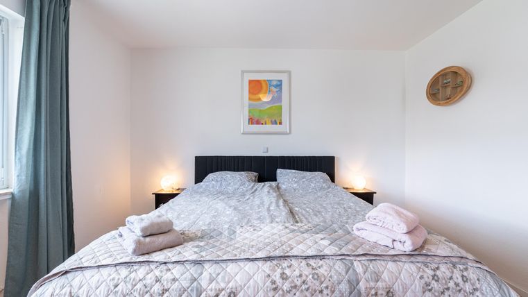 Een gezellige slaapkamer met een groot bed en zachte kussens. Aan de muur hangt een kleurrijk schilderij, en er is zachte verlichting.