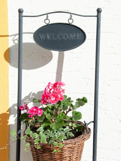 A welcome sign with a basket full of pink flowers. The scene exudes friendliness and hospitality.