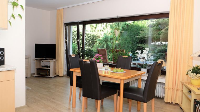 Une salle à manger lumineuse avec une table en bois et des chaises noires. De grandes fenêtres offrent une vue sur un beau jardin.