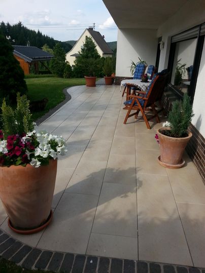 Une terrasse carrelée avec plusieurs pots de plantes. À l'arrière-plan, on peut voir des prairies vertes et des arbres.