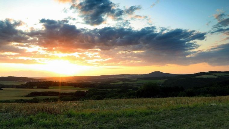 A beautiful sunset over a hilly landscape. The sky is colored vibrantly and the fields are green.