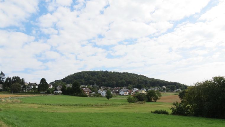A peaceful landscape with gentle hills and a clear sky. In the foreground, lush green grass is visible.