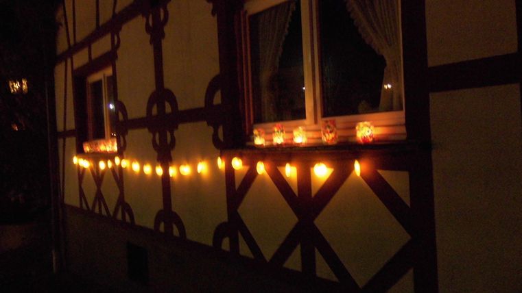 Ein gemütliches Haus mit ausgeleuchteten Fenstern und einer Lichterkette. Die warmen Lichter erzeugen eine einladende Atmosphäre in der Nacht.