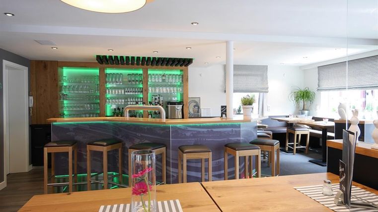 A modern bar with tasteful décor and soft lighting. The seating is comfortable and there are large windows that create a bright atmosphere.