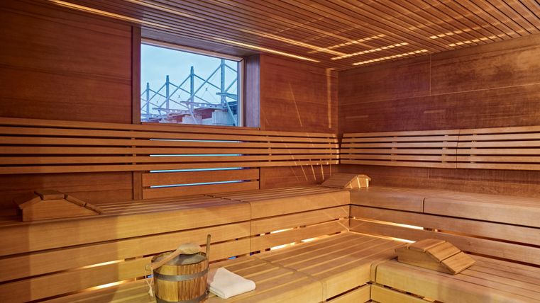 A cozy wooden sauna room with benches in the interior. A construction site view is visible through the window.