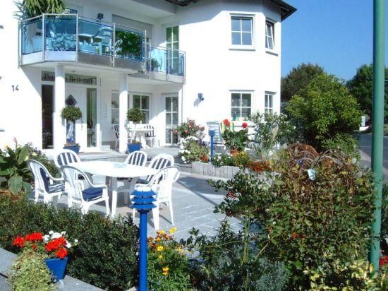 Ein schönes Haus mit einem einladenden Garten. Es gibt eine Terrasse mit weißen Gartenmöbeln und bunten Blumen.