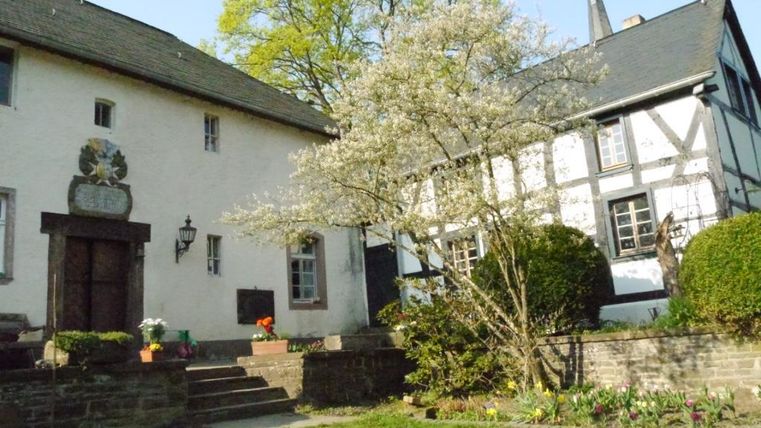 A historic building with a beautiful garden and a blooming tree. In the background, another traditional structure can be seen.