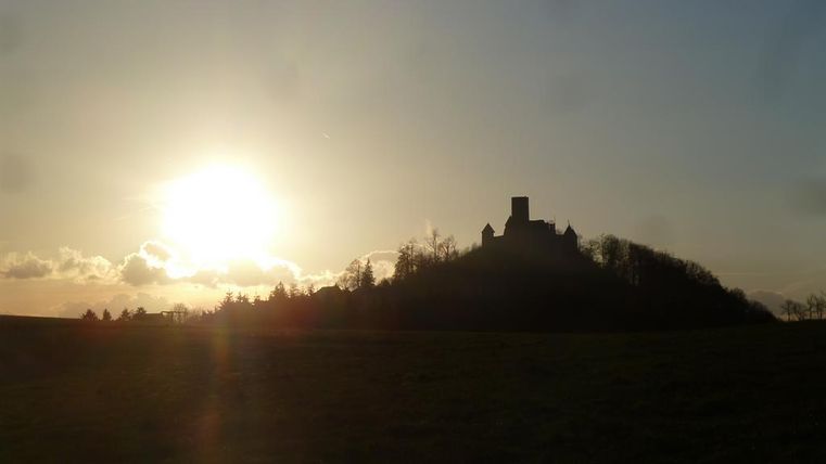 Eine Silhouette einer Burg auf einem Hügel bei Sonnenuntergang. Der Himmel ist klar und die Sonne strahlt am Horizont.