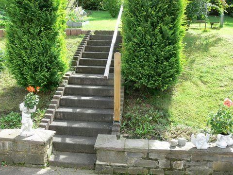 Een stenen trap leidt door een groene tuin. Aan beide zijden van de trap staan goed onderhouden planten en decoratieve figuren.