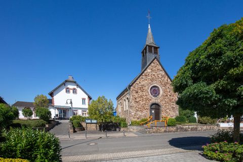Een schilderachtige straat met een kerk en een wit gebouw. De omgeving is groen en zonnig, met een heldere blauwe lucht.