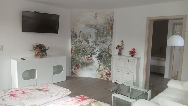 A modern room with two beds, a television, and an elegant coffee table. On the wall is an artistic mural and decorative plants.