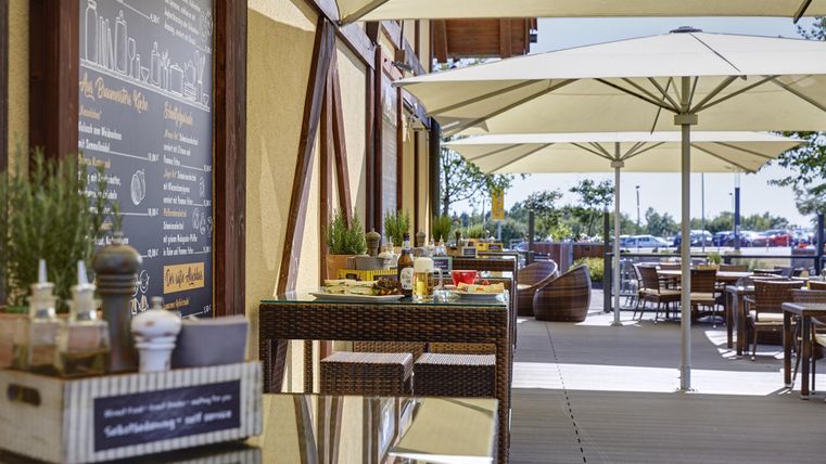 Un restaurant avec des places extérieures confortables et des parasols. Sur une table, des boissons et des collations sont joliment disposées.