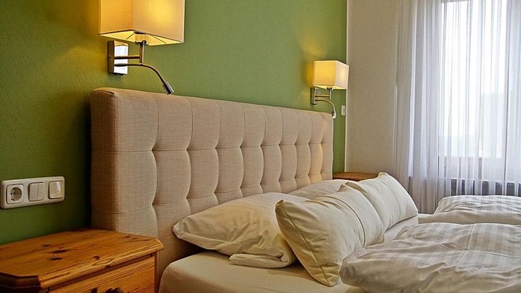 Une chambre confortable avec une tête de lit rembourrée et deux oreillers blancs. Les murs sont peints en vert, et il y a des sources de lumière naturelle à travers la fenêtre.