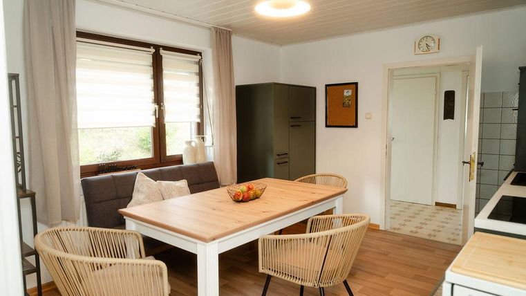 Eine helle Küche mit einem Essbereich, der einen Holztisch und vier Stühle umfasst. Durch die Fenster fällt viel Licht und schafft eine gemütliche Atmosphäre.