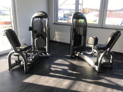 Een moderne sportschool met meerdere trainingsapparaten. De apparaten zijn geplaatst in een heldere ruimte met grote ramen.