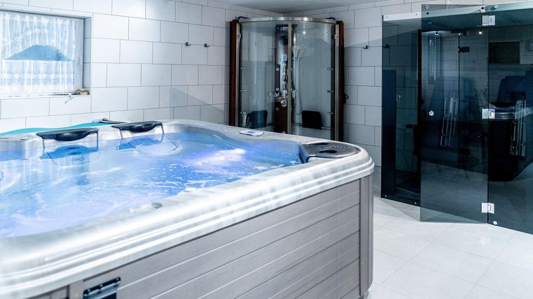 Een luxueuze jacuzzi in een moderne ruimte met witte tegels. Op de achtergrond zijn een douchecabine en grote ramen te zien.