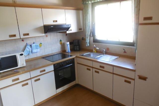 Une cuisine moderne avec des armoires claires et une fenêtre qui laisse entrer beaucoup de lumière. Sur le plan de travail se trouvent un micro-ondes et une machine à café.