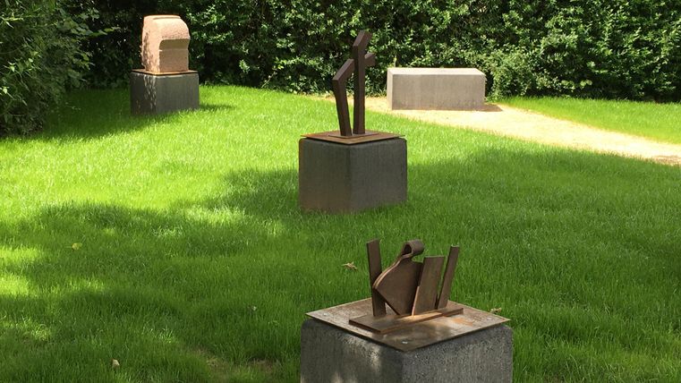 Une pelouse verte avec plusieurs sculptures sur des fondations en béton. À l'arrière-plan, on peut voir des buissons.