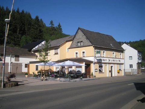 Une auberge pittoresque avec terrasse dans un endroit calme de la rue. Entourée d'arbres et d'un ciel bleu clair.