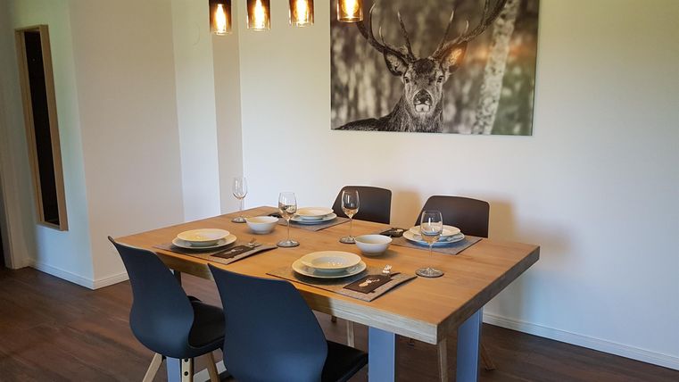 Ein gemütlicher Essbereich mit einem Holzhaustisch und modernen Stühlen. An der Wand hängt ein Kunstwerk mit einem Hirschmotiv.