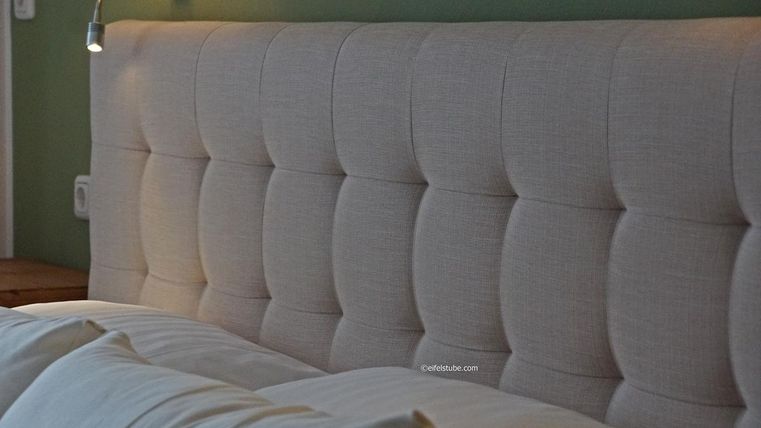 Une tête de lit moderne avec un tissu rembourré en beige clair. Elle se trouve dans une chambre à coucher aux couleurs douces.