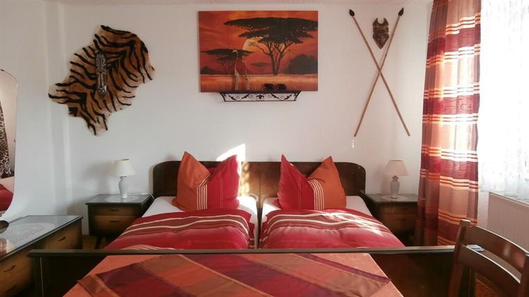 A cozy bedroom with two beds and red pillows. The walls are adorned with African motifs and decorations.
