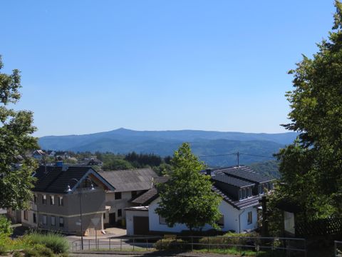 Ein malerisches Dorf in der Natur mit Häusern und Bäumen. Im Hintergrund sind sanfte Hügel unter einem klaren blauen Himmel zu sehen.