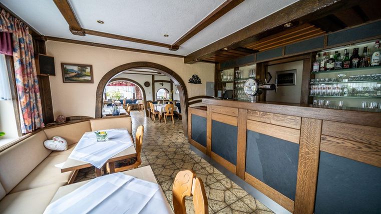 Een gezellig restaurant met houten elementen en een uitnodigende bar. De tafels zijn net gedekt en er heerst een aangename sfeer.