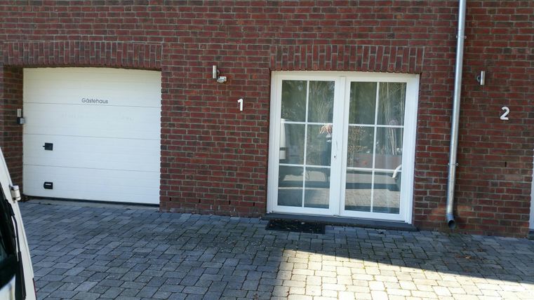 A brick wall with a garage door and a balcony. Next to the balcony, two numbers are visible, 1 and 2.