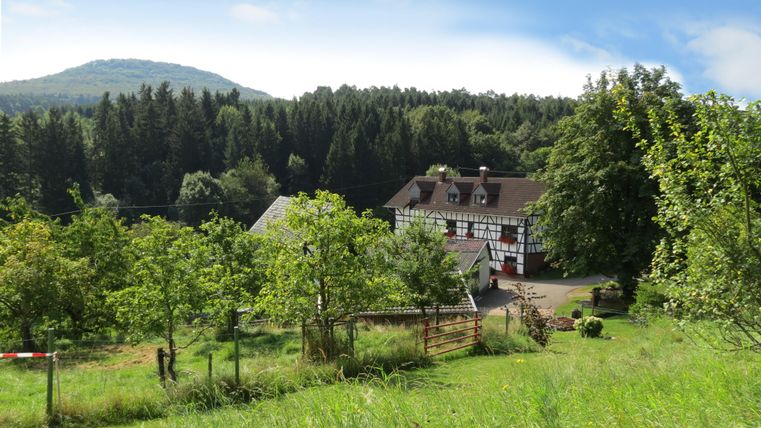 Eine malerische Scheune umgeben von grünen Wiesen und Bäumen. Im Hintergrund sind sanfte Hügel zu sehen.