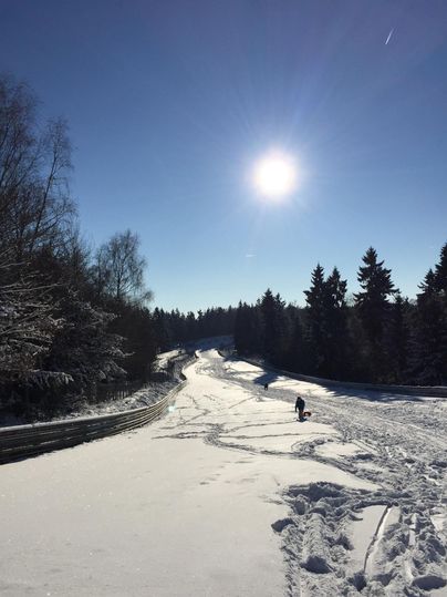 Eine verschneite Landschaft unter einem klaren blauen Himmel. Im Hintergrund ist ein schmaler Weg und ein Sonnenstrahl zu sehen.