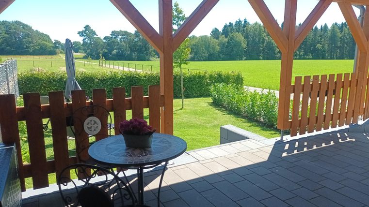 Een uitnodigende buitenruimte met een ronde tafel en stoelen. Op de achtergrond is een groene grasveld en een blauwe lucht te zien.