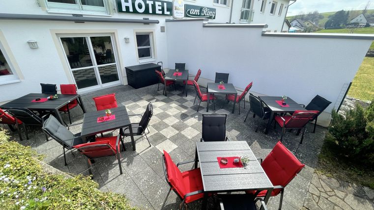 Een uitnodigend terras voor een hotel met zwart-rode tafels en stoelen. De omgeving is groen en biedt een gezellige plek buiten.